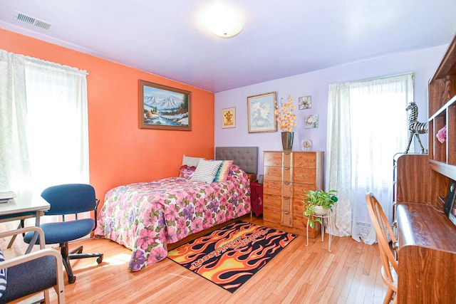 bedroom with hardwood / wood-style floors, multiple windows, and visible vents