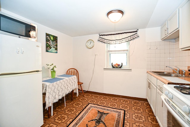 kitchen with tasteful backsplash, baseboards, tile patterned floors, white appliances, and a sink