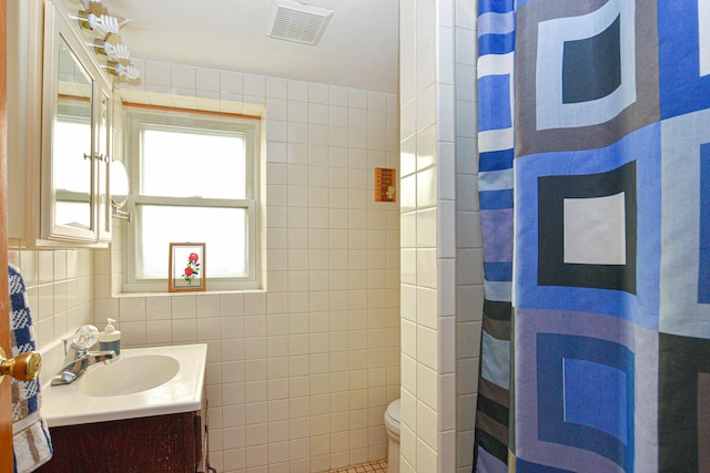 full bathroom with visible vents, toilet, vanity, a shower with shower curtain, and tile walls