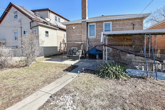 rear view of property featuring brick siding, a chimney, a patio, and fence