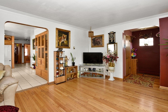 living room with crown molding, baseboards, arched walkways, and light wood-type flooring