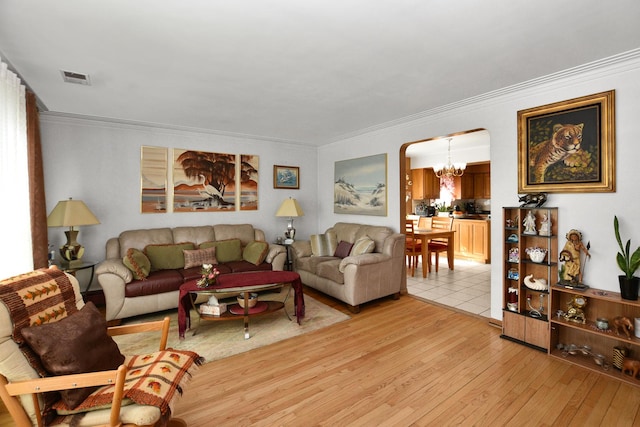 living area featuring visible vents, arched walkways, ornamental molding, light wood-style floors, and a chandelier