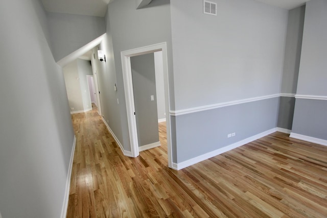 hallway featuring visible vents, baseboards, and light wood finished floors