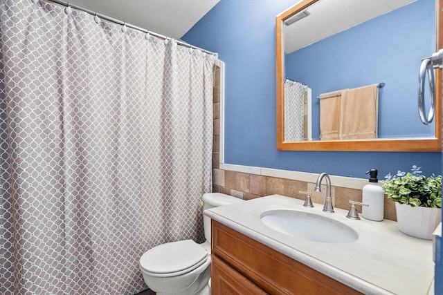 full bath with a wainscoted wall, toilet, a shower with curtain, tile walls, and vanity