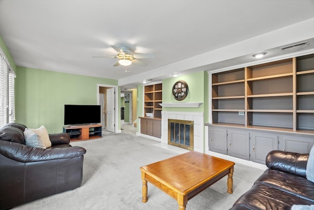 living room with visible vents, light carpet, built in shelves, a ceiling fan, and a tile fireplace