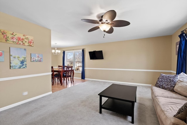 carpeted living area with ceiling fan with notable chandelier and baseboards