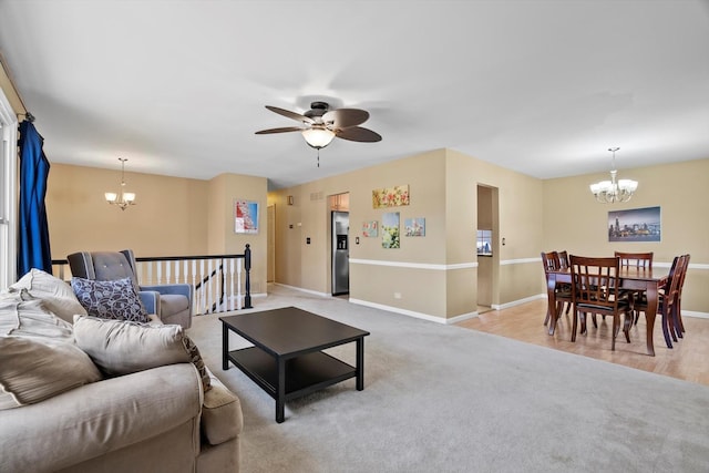 living area with light colored carpet, ceiling fan with notable chandelier, and baseboards