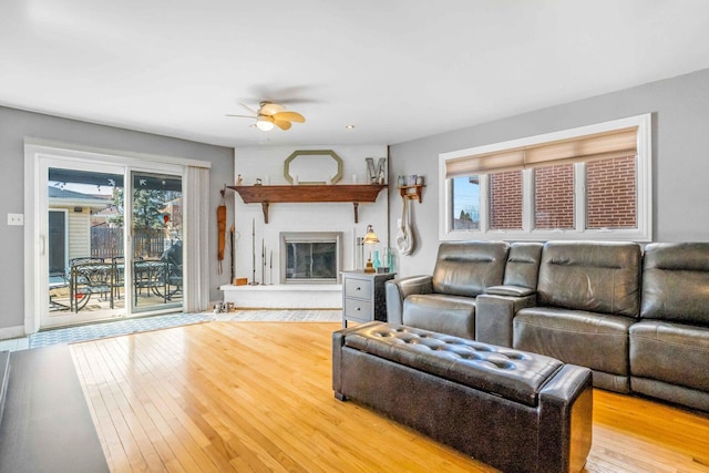 living area featuring baseboards, ceiling fan, a fireplace, and hardwood / wood-style flooring