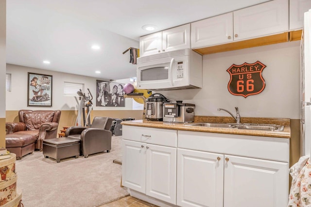 kitchen featuring white microwave, light carpet, white cabinetry, and a sink