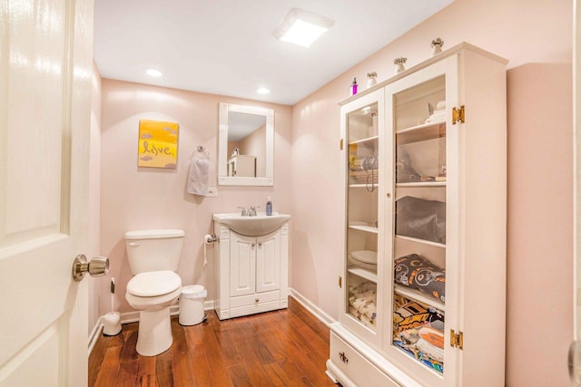 half bathroom with toilet, wood finished floors, recessed lighting, baseboards, and vanity