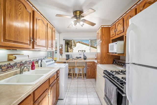 kitchen with light countertops, light tile patterned floors, brown cabinetry, white appliances, and a sink