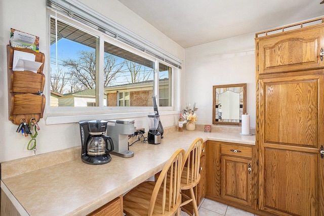 kitchen featuring light tile patterned floors, brown cabinetry, light countertops, and built in study area