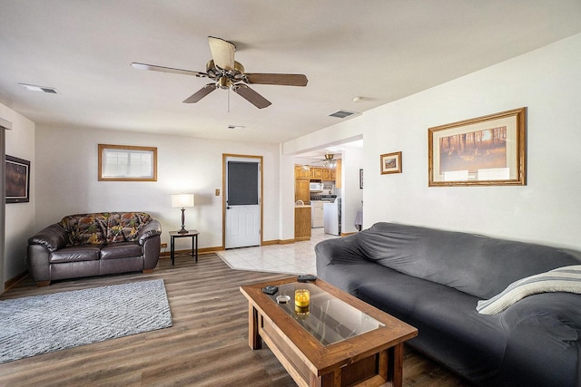 living room featuring light wood finished floors, visible vents, baseboards, and a ceiling fan