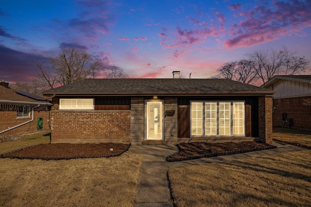 single story home featuring a lawn, brick siding, and roof with shingles