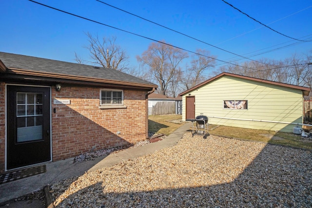 view of side of home featuring brick siding, roof with shingles, and fence