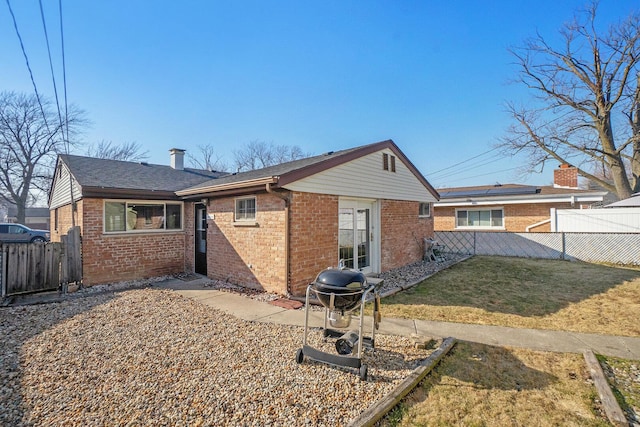 back of property featuring a chimney, fence, brick siding, and a lawn