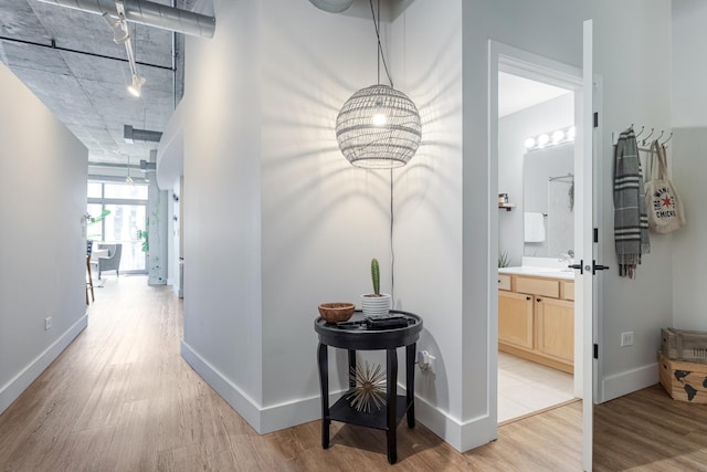 hall featuring light wood finished floors, rail lighting, and baseboards