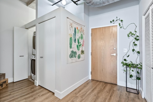 entryway with light wood-style flooring, stacked washer and clothes dryer, and baseboards