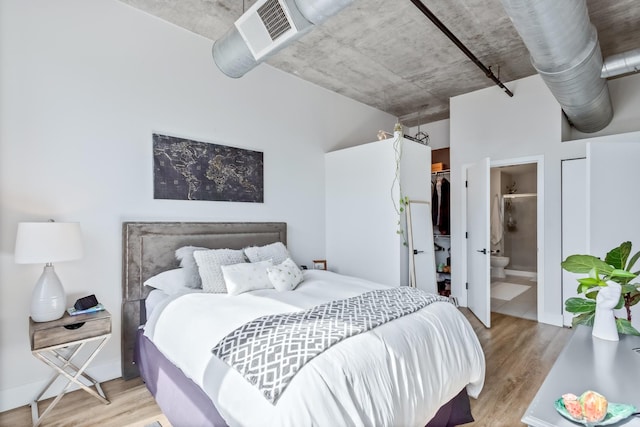 bedroom with a closet, ensuite bath, wood finished floors, and a spacious closet