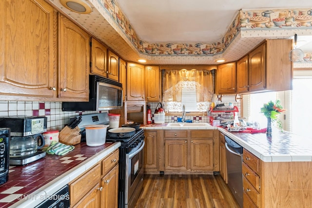 kitchen featuring tile countertops, wood finished floors, stainless steel appliances, a raised ceiling, and a sink