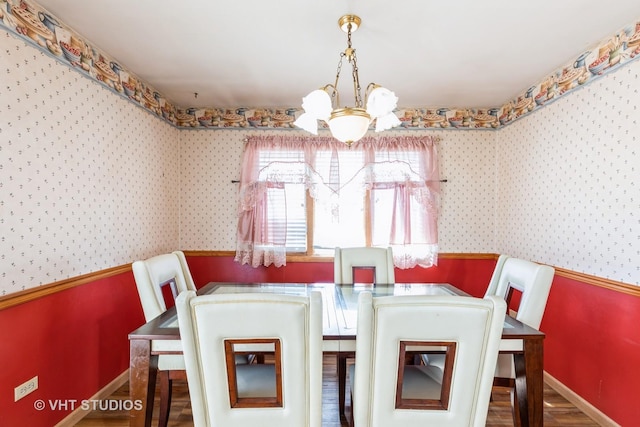 dining room featuring wood finished floors, baseboards, wallpapered walls, wainscoting, and a notable chandelier