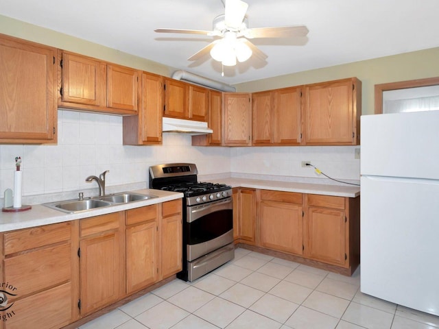 kitchen with freestanding refrigerator, a sink, under cabinet range hood, gas range, and backsplash