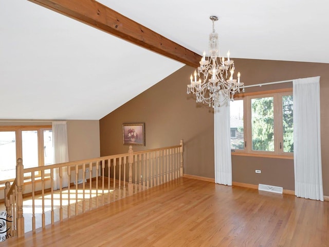 empty room featuring a healthy amount of sunlight, lofted ceiling with beams, baseboards, and wood finished floors