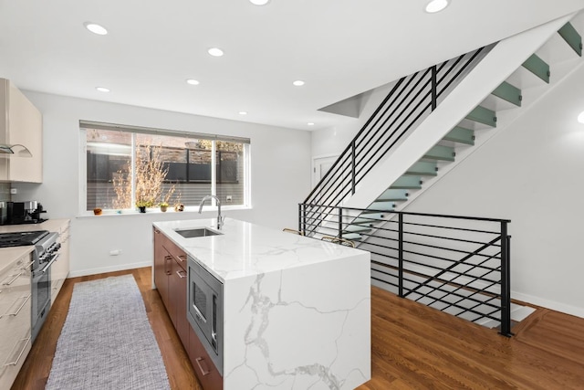 kitchen featuring an island with sink, wood finished floors, stainless steel appliances, and a sink