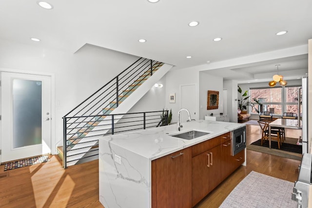 kitchen featuring a sink, stainless steel microwave, wood finished floors, and a kitchen island with sink