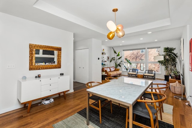 dining area featuring a notable chandelier, recessed lighting, a raised ceiling, and wood finished floors