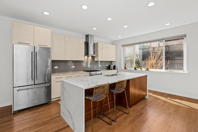 kitchen featuring modern cabinets, high end fridge, a sink, wood finished floors, and wall chimney exhaust hood