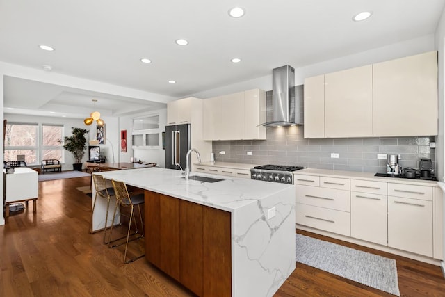 kitchen featuring dark wood-style floors, high end refrigerator, wall chimney range hood, and a sink