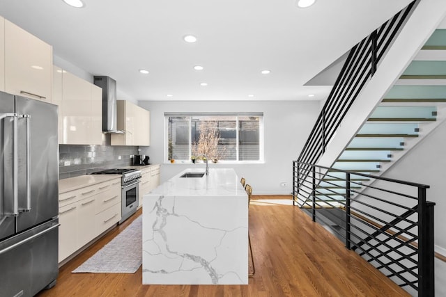 kitchen featuring high quality appliances, light wood finished floors, a sink, wall chimney exhaust hood, and modern cabinets