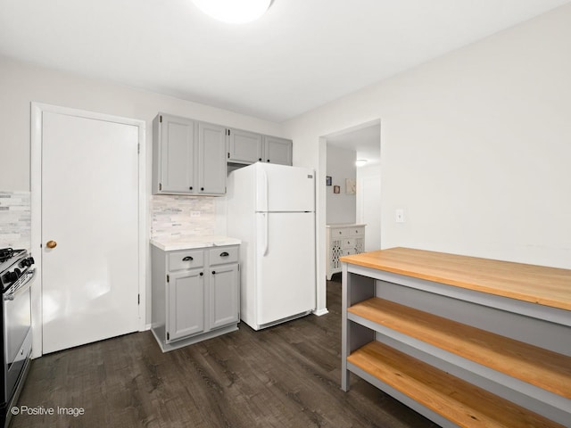 kitchen featuring dark wood-type flooring, gas stove, tasteful backsplash, and freestanding refrigerator