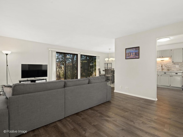 living area with dark wood finished floors, a chandelier, and baseboards