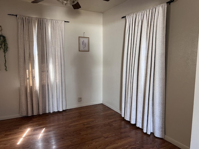 empty room featuring baseboards, dark wood-style floors, and a ceiling fan