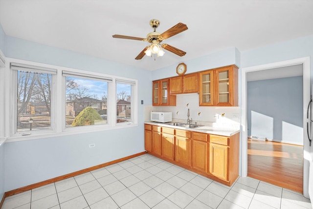 kitchen featuring white microwave, a sink, light countertops, glass insert cabinets, and brown cabinets