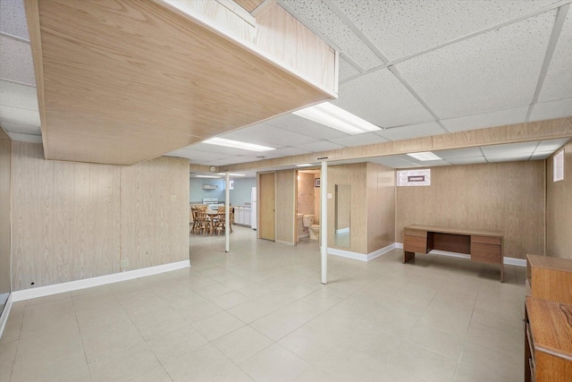 below grade area featuring a paneled ceiling, baseboards, and wood walls