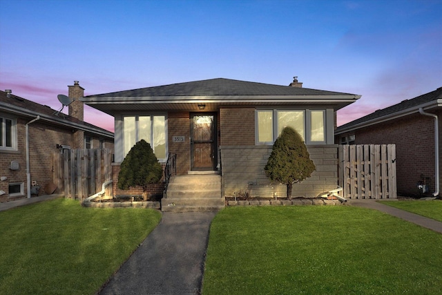 bungalow-style home featuring brick siding, a lawn, and fence