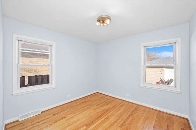 empty room with a wealth of natural light, visible vents, baseboards, and wood finished floors