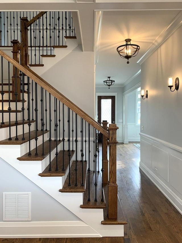 stairway featuring visible vents, ornamental molding, wainscoting, wood finished floors, and a decorative wall