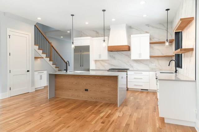 kitchen with premium range hood, open shelves, stainless steel built in refrigerator, and a sink