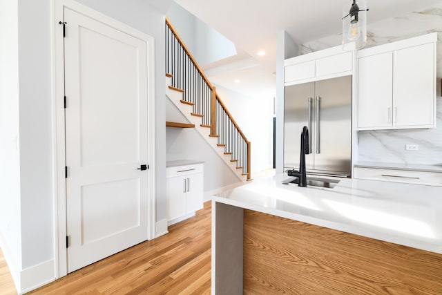 kitchen with a sink, stainless steel built in fridge, light countertops, white cabinets, and light wood-type flooring