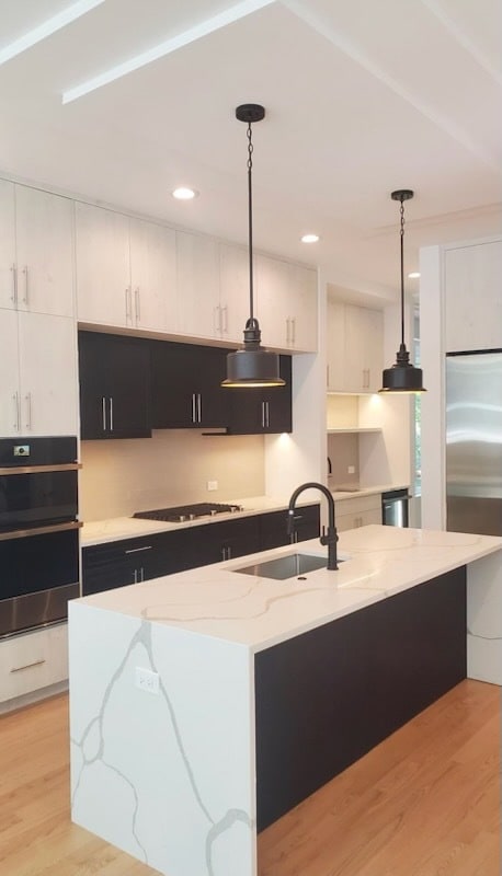 kitchen with light wood-style flooring, an island with sink, multiple ovens, and stainless steel built in fridge