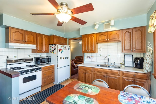 kitchen featuring under cabinet range hood, brown cabinets, white appliances, and a sink