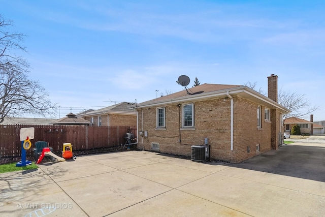 back of property featuring a patio, central AC, fence, brick siding, and a chimney