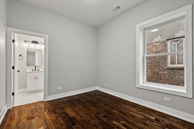 unfurnished bedroom featuring connected bathroom, visible vents, baseboards, and dark wood finished floors