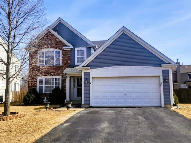 traditional-style house with brick siding, an attached garage, driveway, and fence