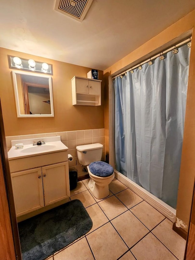 full bath featuring tile patterned floors, visible vents, a wainscoted wall, toilet, and tile walls