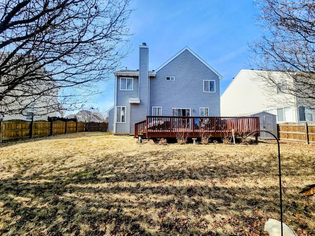 rear view of house featuring a shed, a chimney, a deck, a fenced backyard, and an outbuilding